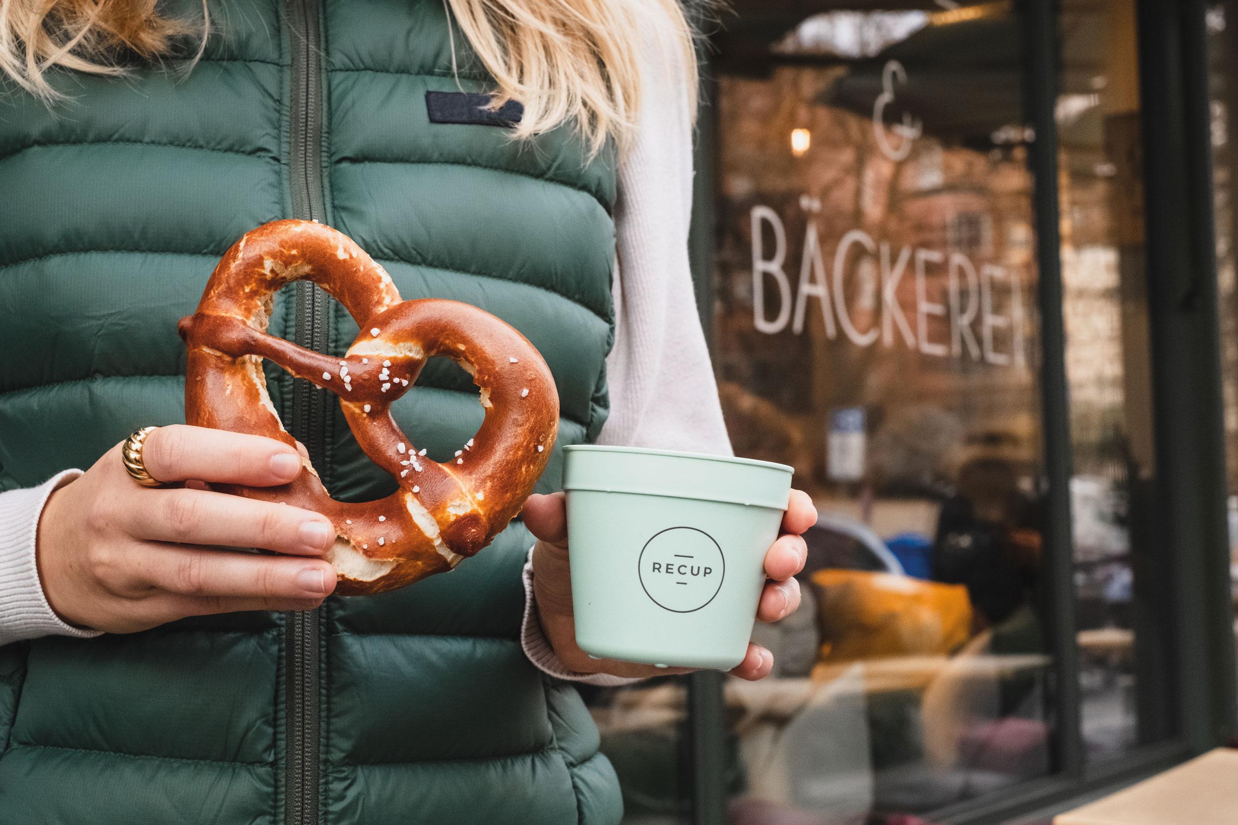 Person holding a reusable cup and a pretzel